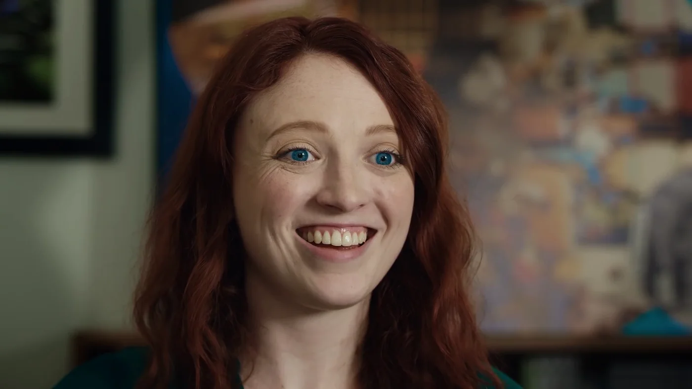 A smiling red-haired woman in an interview shot from Bad News.