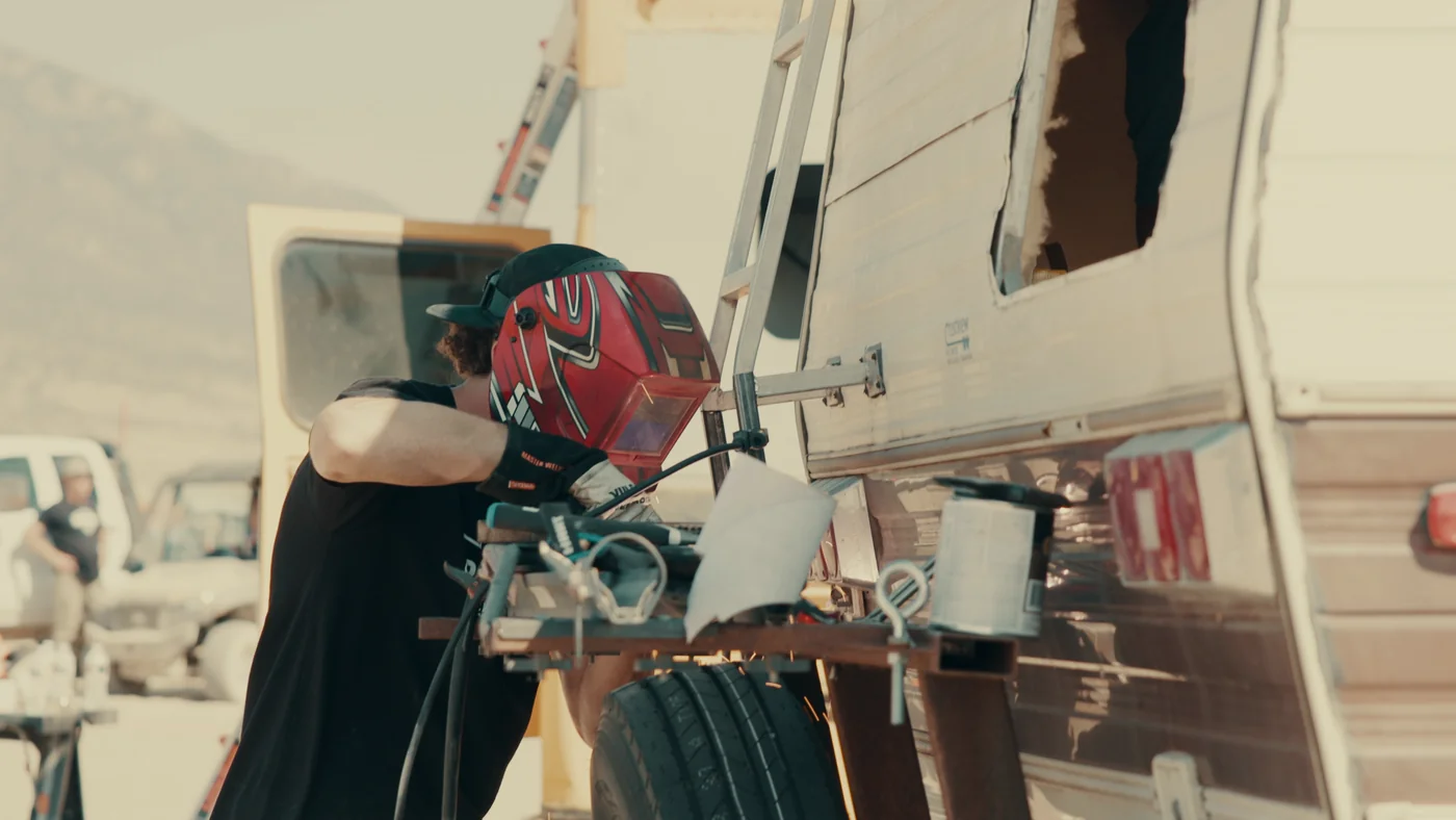 A contestant in a welding helmet works beside a motorhome in Gutted season one.