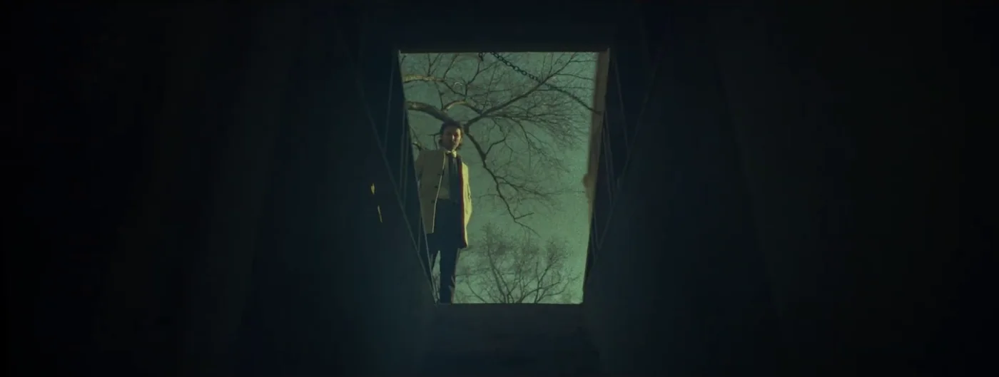 Seen from below, a man in a tan coat stands at the open door of a cellar in Justice for Peanut.