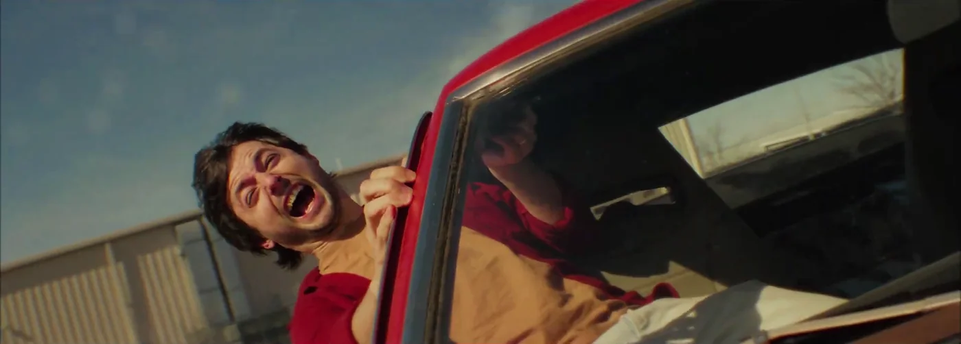 A man yells out the window of a red car in Kings of KC.