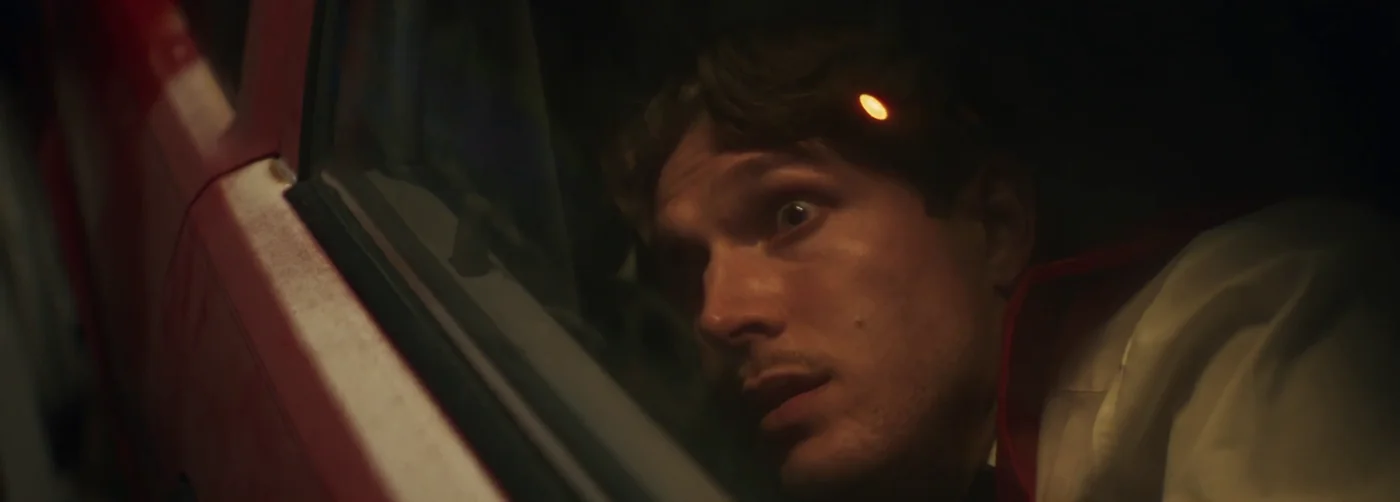 A man peers wide-eyed through a car window at night in Kings of KC.