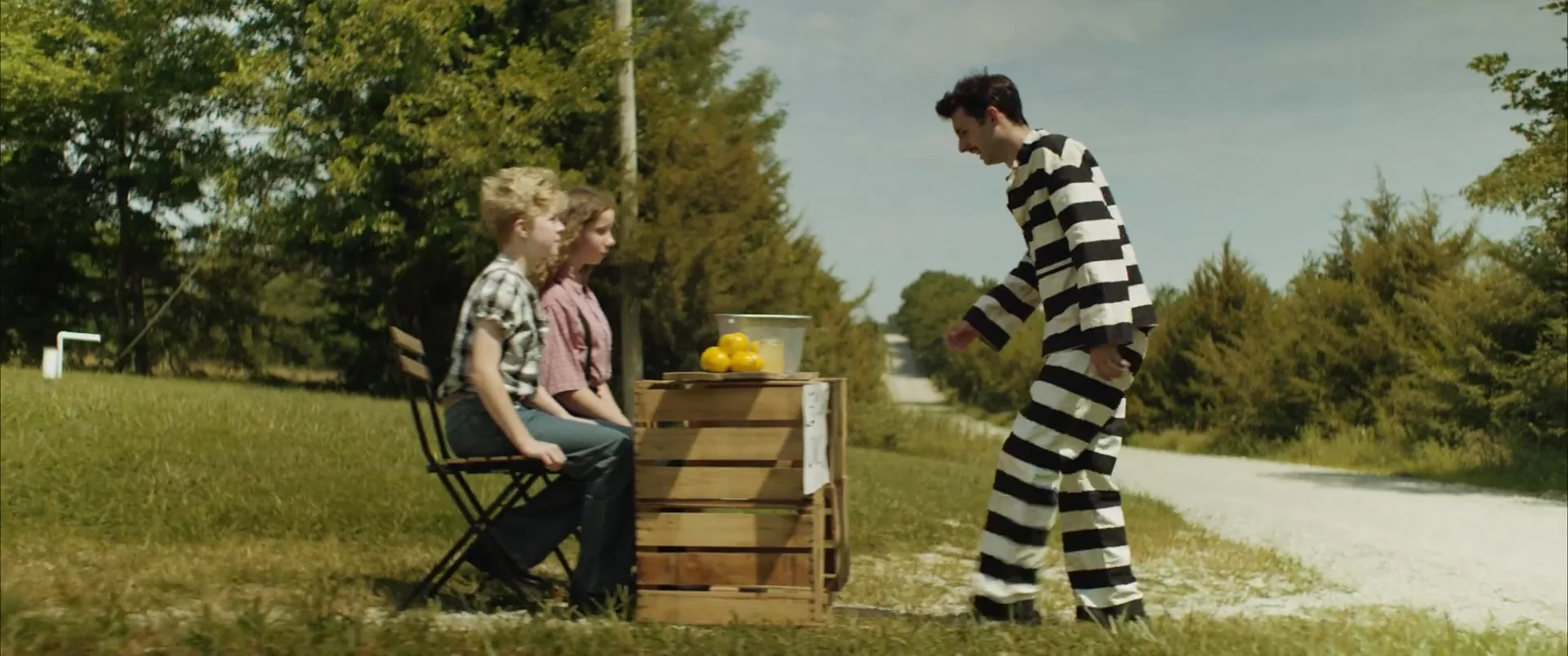 A man in a striped prison uniform approaches two children at a roadside lemonade stand in The Escape of Tina Kleinfelder.