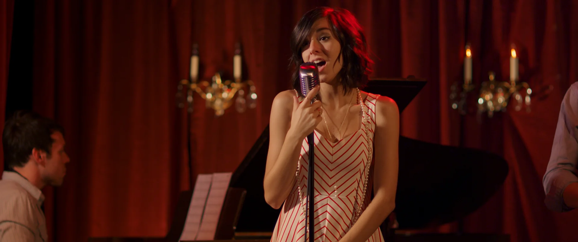 A singer performs at a microphone against red curtains in The Matchbreaker.